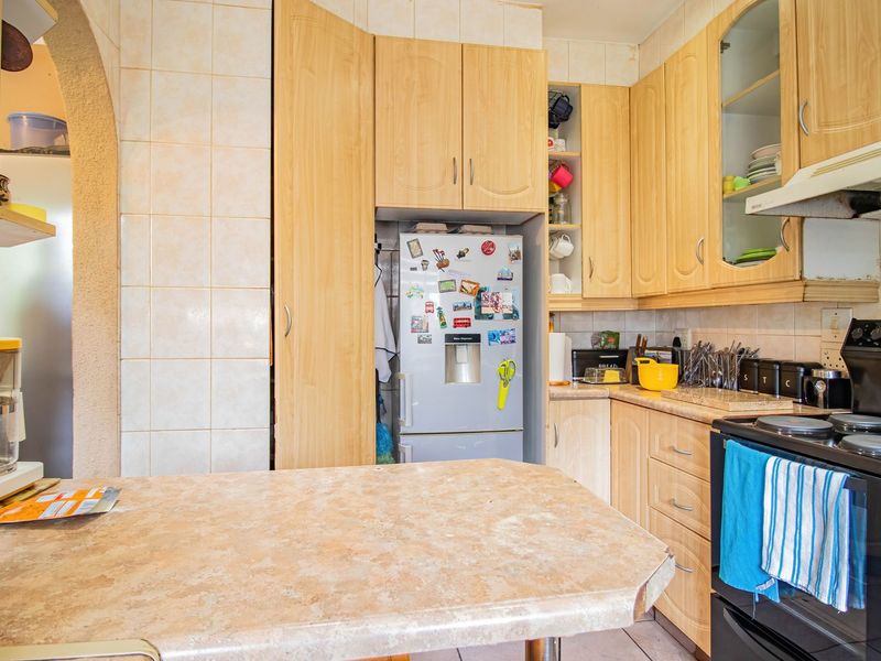 A functional kitchen featuring light wood-tone cabinetry, laminate countertops, a tiled backsplash, and an integrated extractor fan.