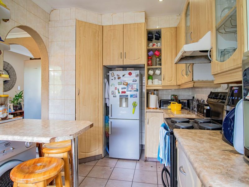 A functional kitchen featuring light wood-tone cabinetry, laminate countertops, tiled backsplash, and integrated cooking appliances, with an open archway leading to adjacent living space.