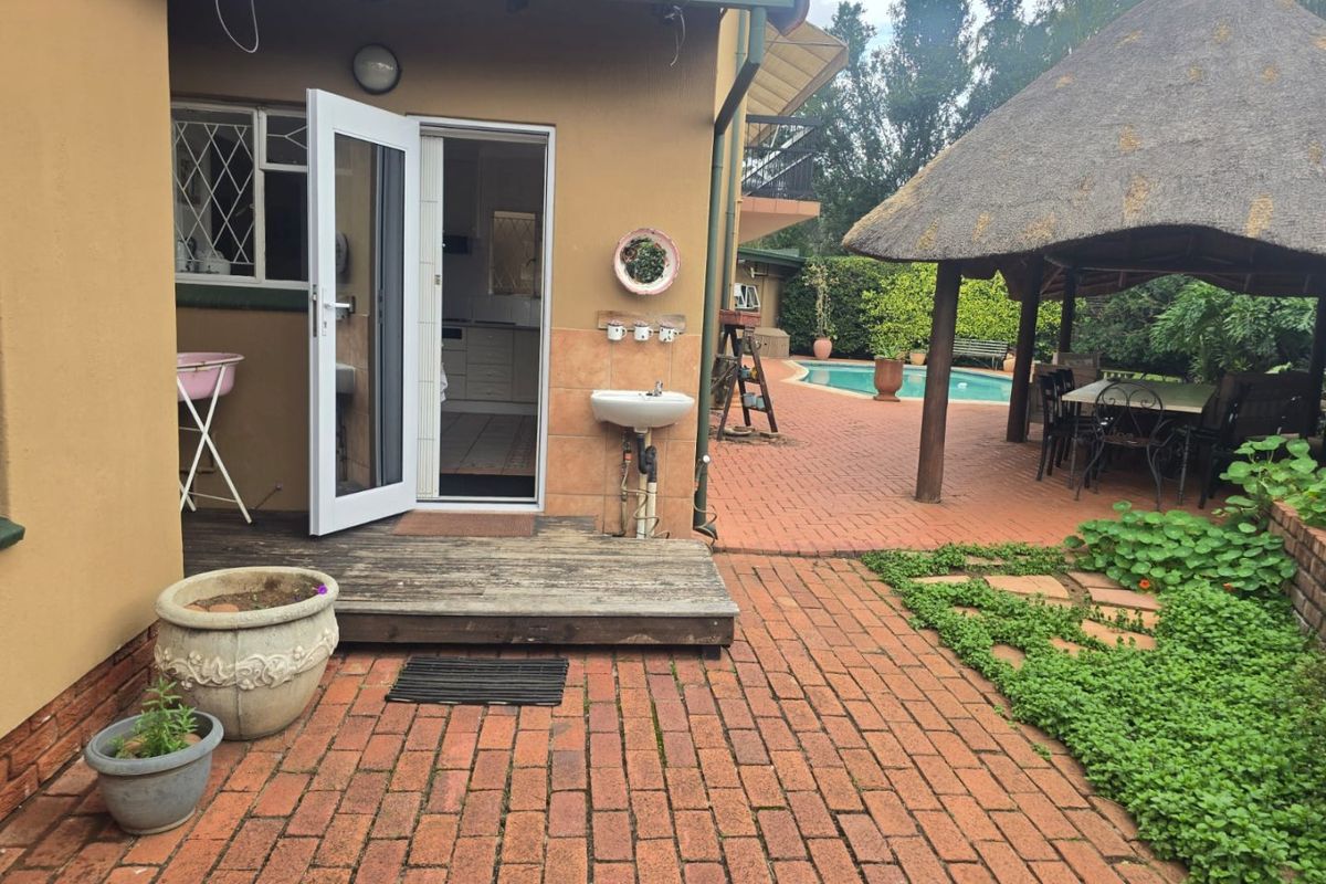 Rear garden area featuring a swimming pool, thatched gazebo, brick paved patio, and timber decking leading into the home.