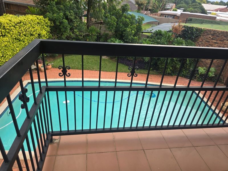 Elevated balcony featuring a metal balustrade overlooking a private swimming pool and landscaped garden area.