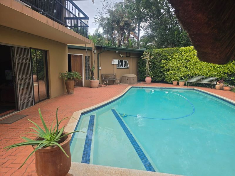 A backyard pool area featuring a swimming pool with integrated steps, brick paving, and access to the main house via sliding doors and a balcony.