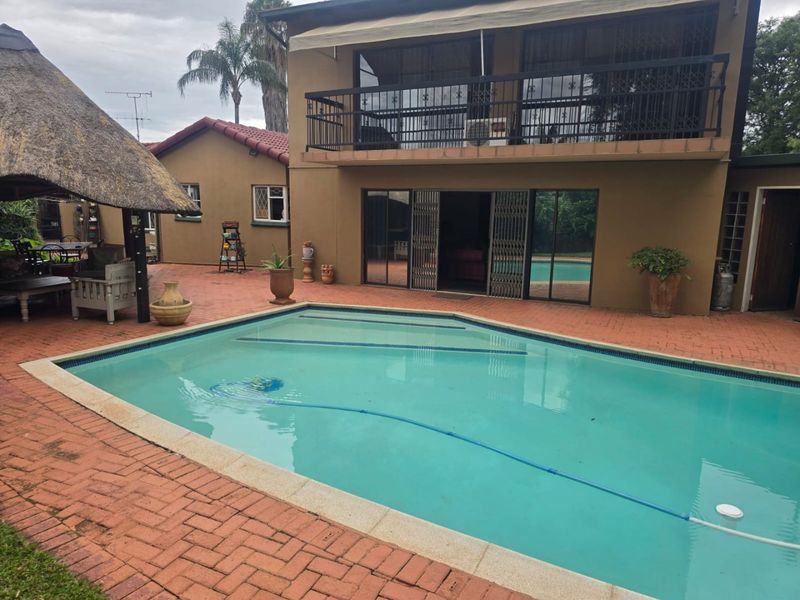 Rear exterior view featuring a swimming pool, brick paved patio area, and a covered thatched lapa, with access to the main house via sliding doors.