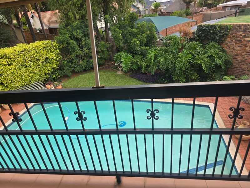 Elevated view overlooking a private swimming pool, paved patio area, and established garden with mature landscaping and brick boundary walls.