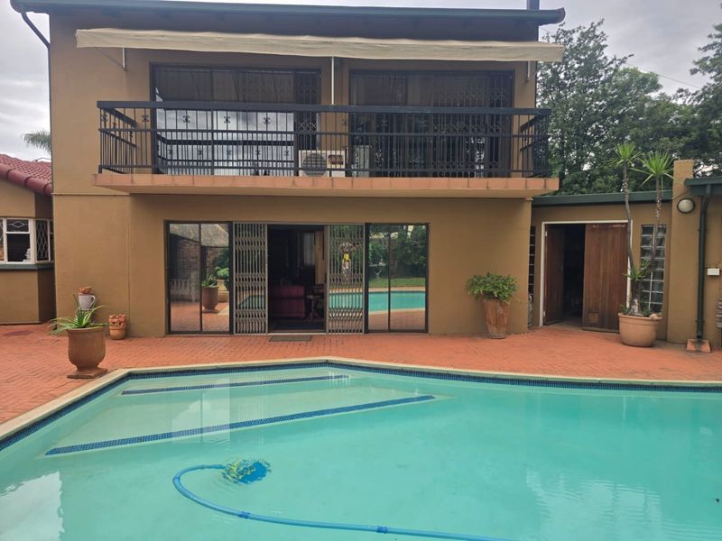 Rear exterior view featuring a swimming pool, brick paved patio, and a balcony with metal security railings and a retractable awning.