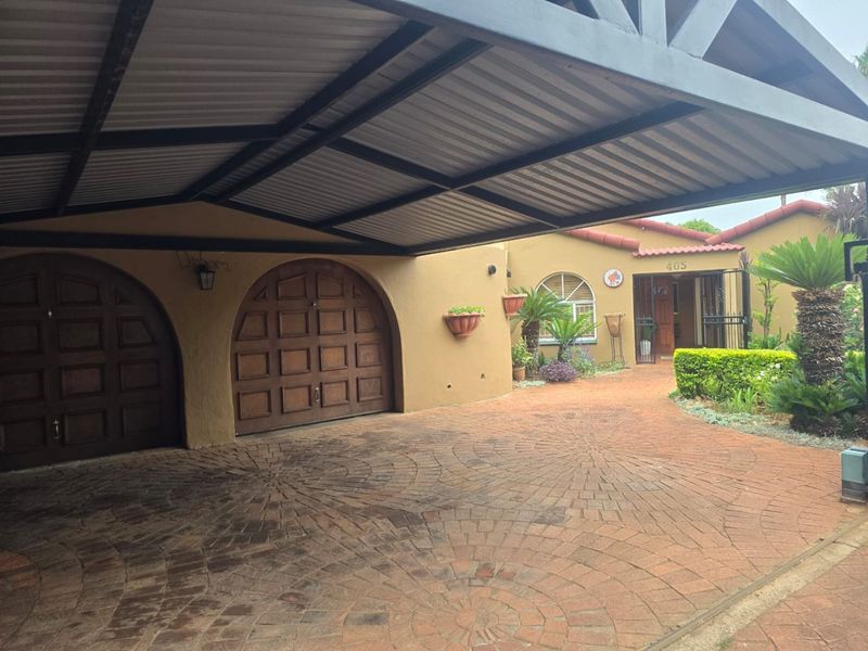 Front exterior view featuring a covered carport, brick paved driveway, arched wooden garage doors, and a well-maintained entrance area.