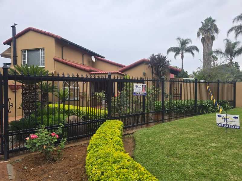 Front view of a residential house featuring a well-maintained garden, wrought iron fencing, and a tiled roof facade.