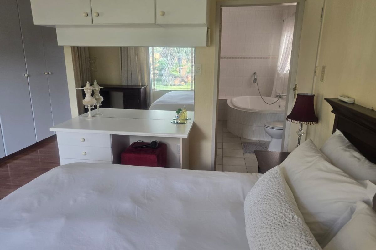 A bedroom featuring built-in cupboards, a vanity area, and an adjoining en-suite bathroom with a corner bathtub.