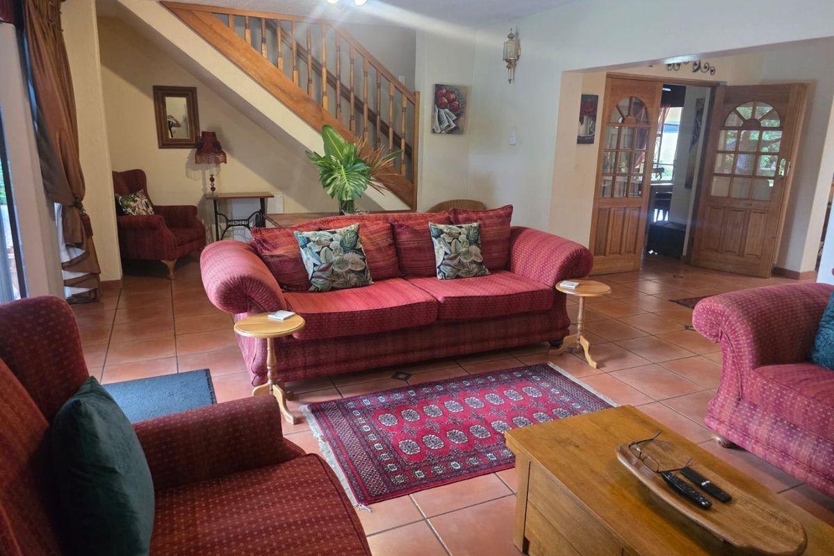 Spacious living room featuring terracotta floor tiles, a wooden staircase with balustrade, and double wooden doors leading to an adjacent room.