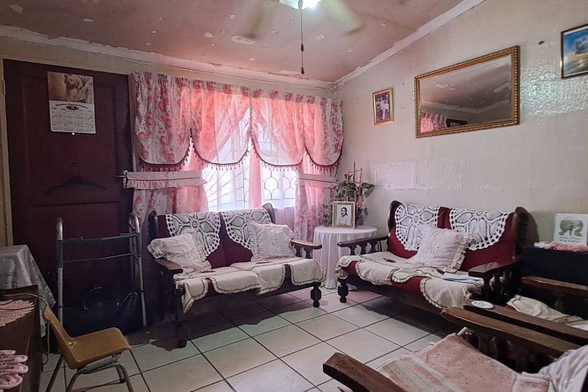 A living room featuring tiled flooring and a ceiling fan, currently showing significant wear to the ceiling and wall finishes.