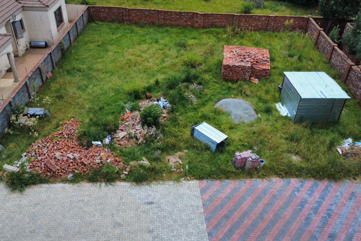 Aerial view of a vacant residential plot featuring a paved driveway, brick boundary walls, and a metal storage shed on site.
