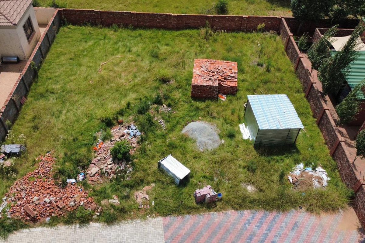 Aerial view of a vacant residential plot featuring perimeter brick walls and existing construction materials on site.