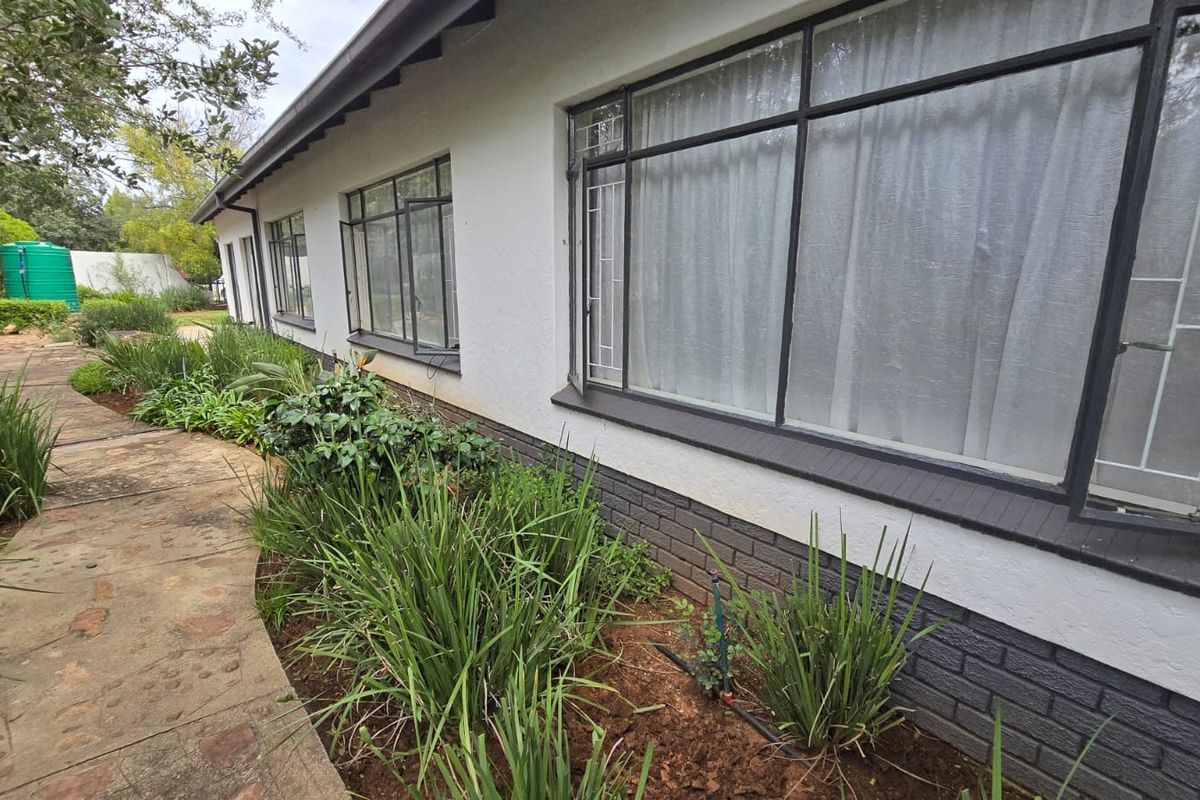 Rear exterior view of the house featuring a stone paved walkway, landscaped garden beds, and steel-framed windows along the plastered brick facade.