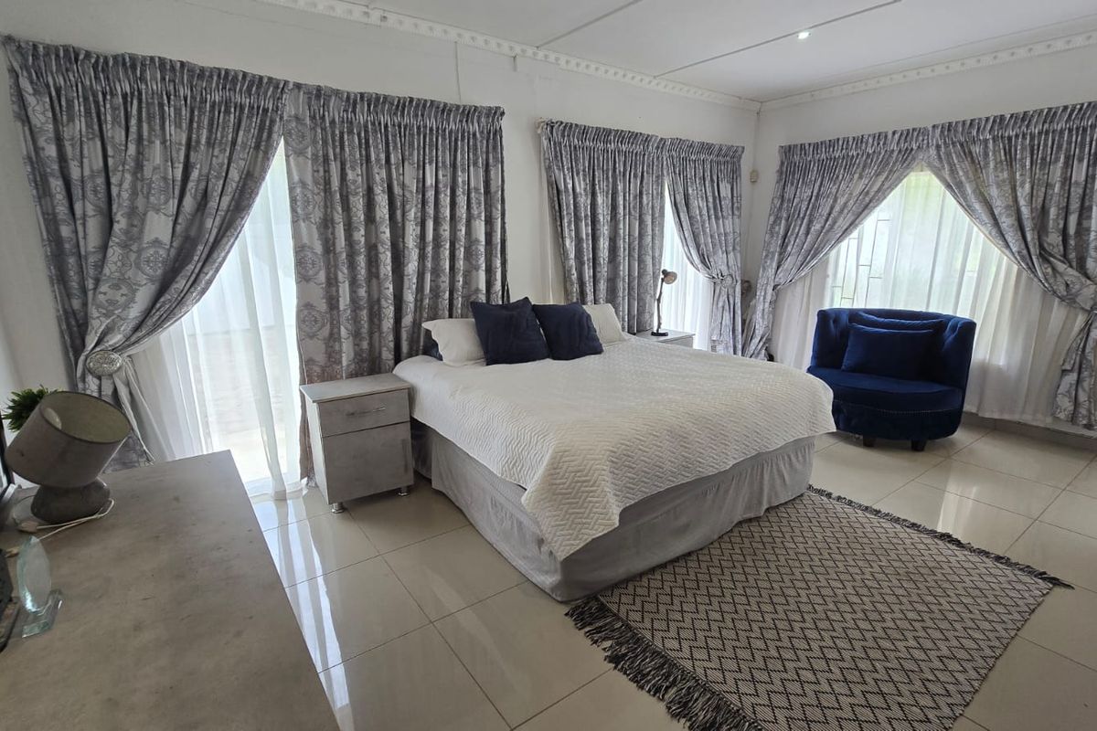 Spacious bedroom featuring neutral tiled flooring, decorative ceiling cornicing, and large windows with floor-to-ceiling curtains allowing for ample natural light.