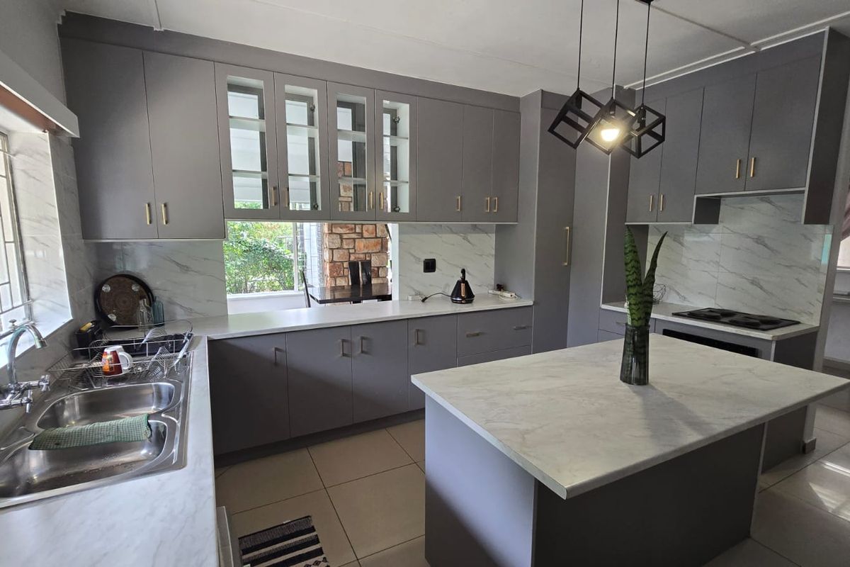 Modern kitchen featuring grey cabinetry, marble-look countertops, a central island, and a double basin sink with ample storage and contemporary pendant lighting.