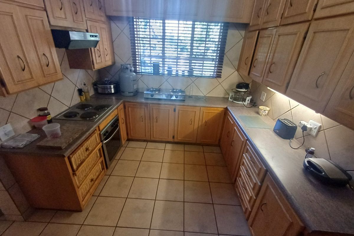A functional U-shaped kitchen featuring traditional wooden cabinetry, laminate countertops, tiled flooring, and a built-in oven with an electric hob.