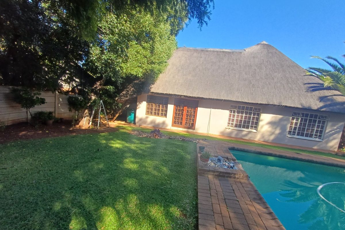 Rear exterior view featuring a swimming pool, brick paved surround, and a house with a traditional thatch roof and timber-framed windows.