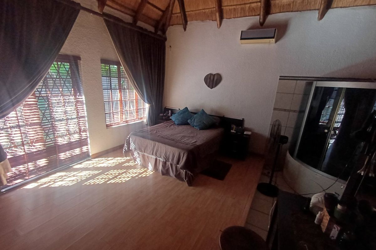 Spacious bedroom featuring a high thatched ceiling with exposed rafters, tiled flooring, integrated air conditioning, and an en-suite shower area.