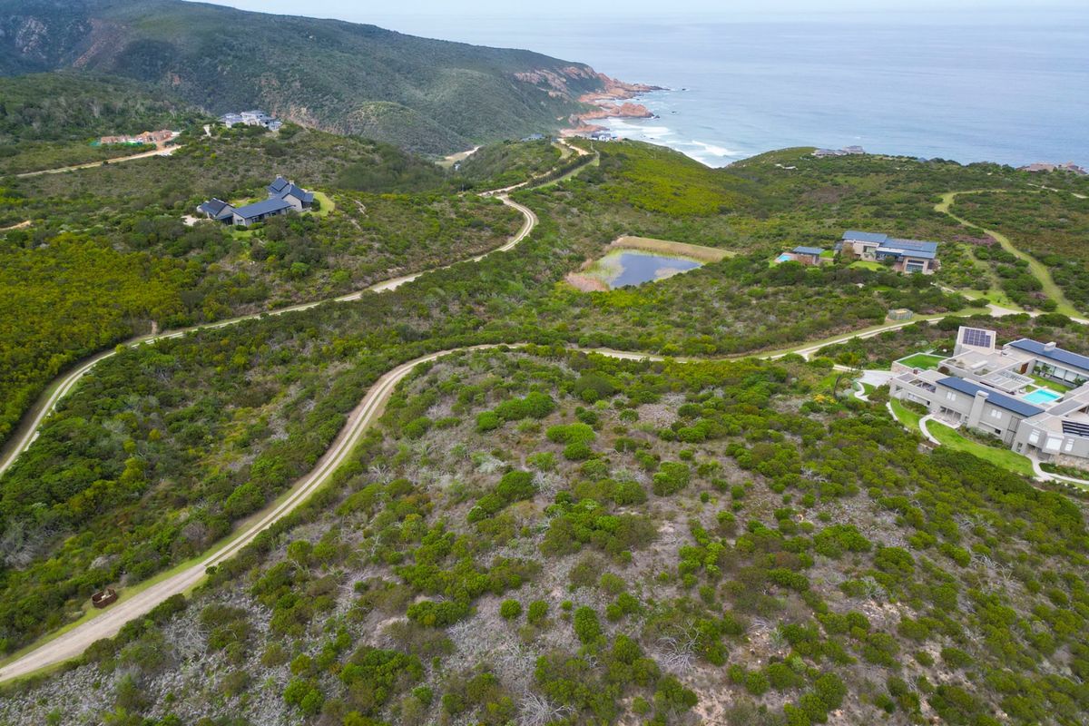 An aerial view of a vacant residential plot featuring natural coastal vegetation, an unpaved access road, and proximity to the ocean.