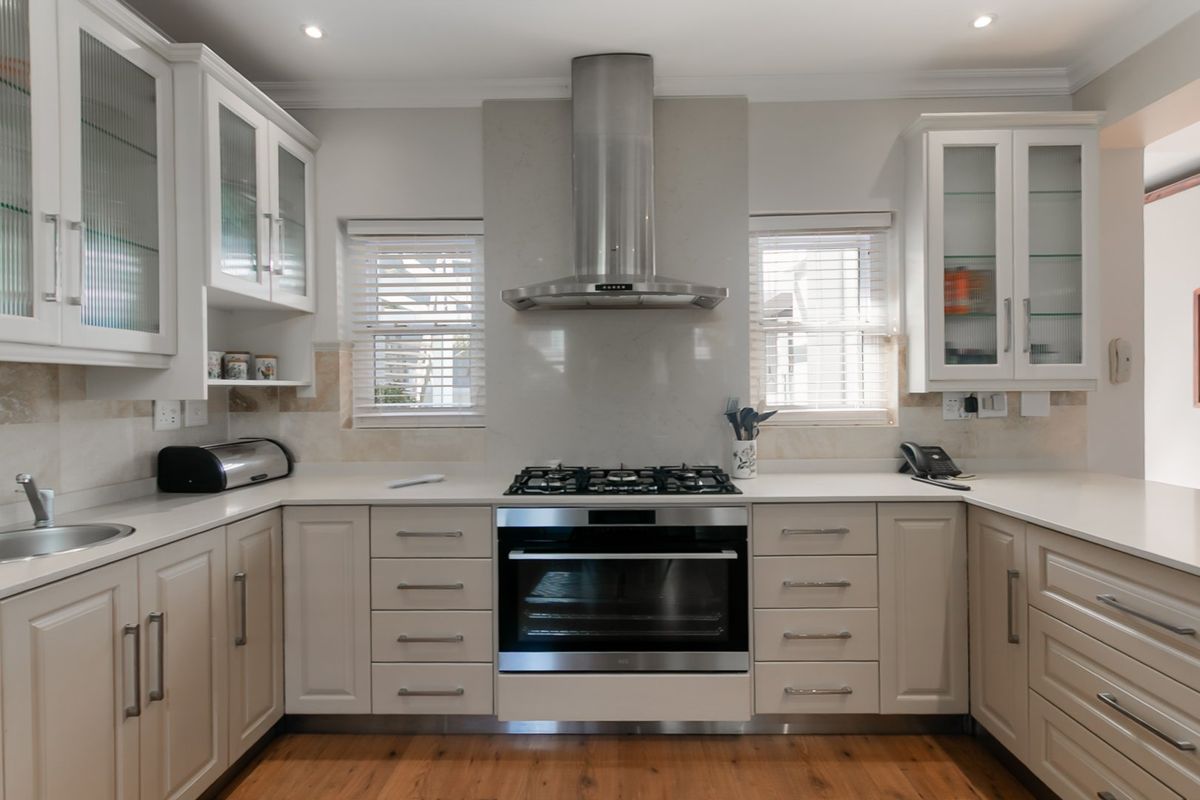 A well-maintained kitchen featuring white cabinetry, stone countertops, stainless steel appliances, and a gas hob with a modern extractor fan.