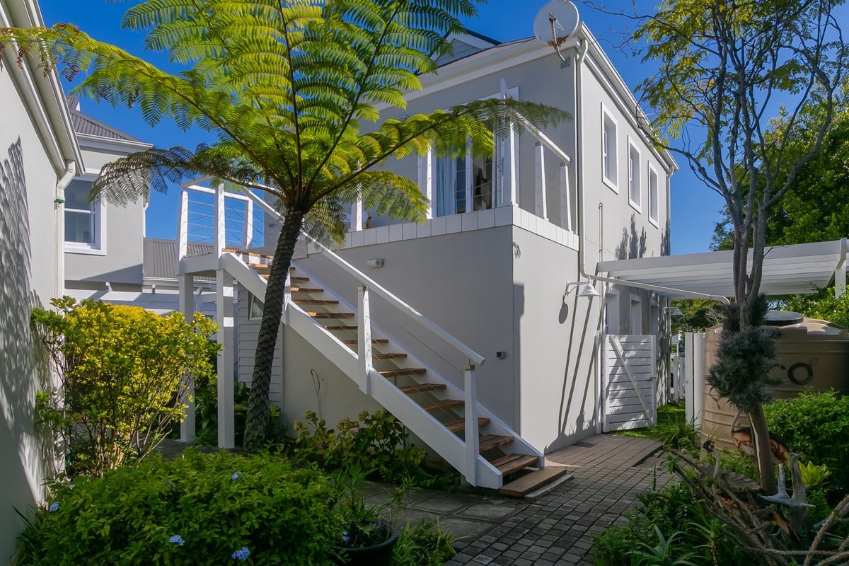 Rear exterior view of the property featuring a paved garden area, external staircase leading to an upper balcony, and a water tank.