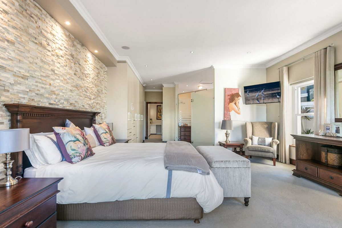 Spacious master bedroom featuring a textured stacked stone accent wall, recessed lighting, built-in cabinetry, and an integrated en-suite bathroom with a glass partition.