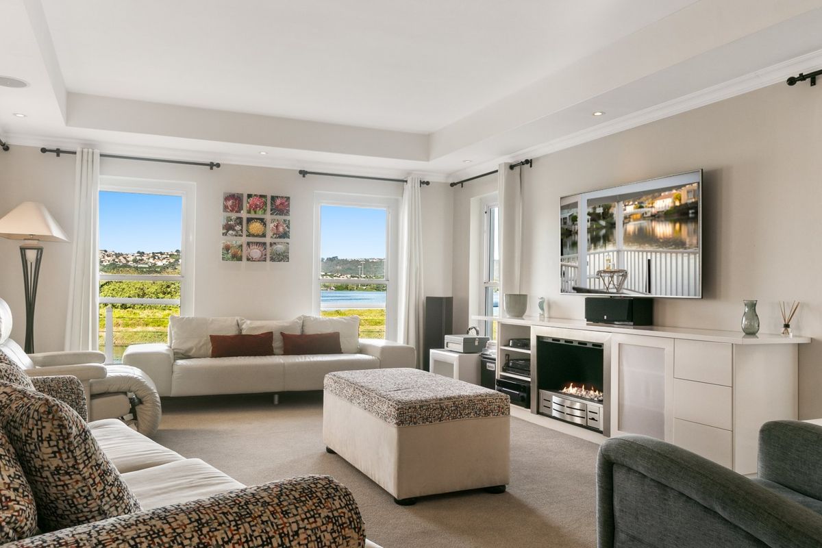 Spacious living room featuring a built-in gas fireplace, custom cabinetry, recessed ceiling with downlights, and large windows offering scenic water views.