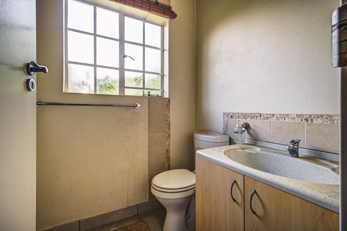 A functional bathroom featuring a vanity with basin, toilet, and tiled splashback, requiring cosmetic updates to improve its overall condition and aesthetic appeal.