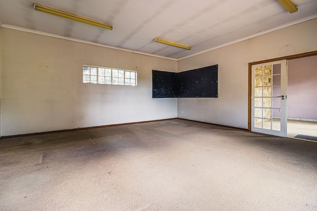 An empty, spacious room featuring carpeted flooring, fluorescent lighting, and a glass-paneled french door leading to an adjacent area.