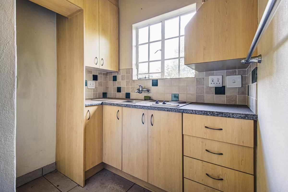 A compact kitchen featuring light wood-finish cabinetry, a tiled backsplash, and a built-in hob, offering a functional prep space.