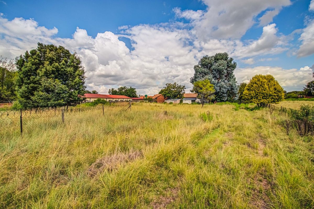 A wide view of the farm property grounds featuring overgrown grass, mature trees, and perimeter razor wire fencing with distant outbuildings.