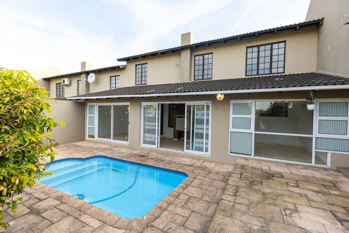 Rear view of the townhouse featuring a private swimming pool, paved patio area, and multiple sliding glass doors providing access to the interior living space.