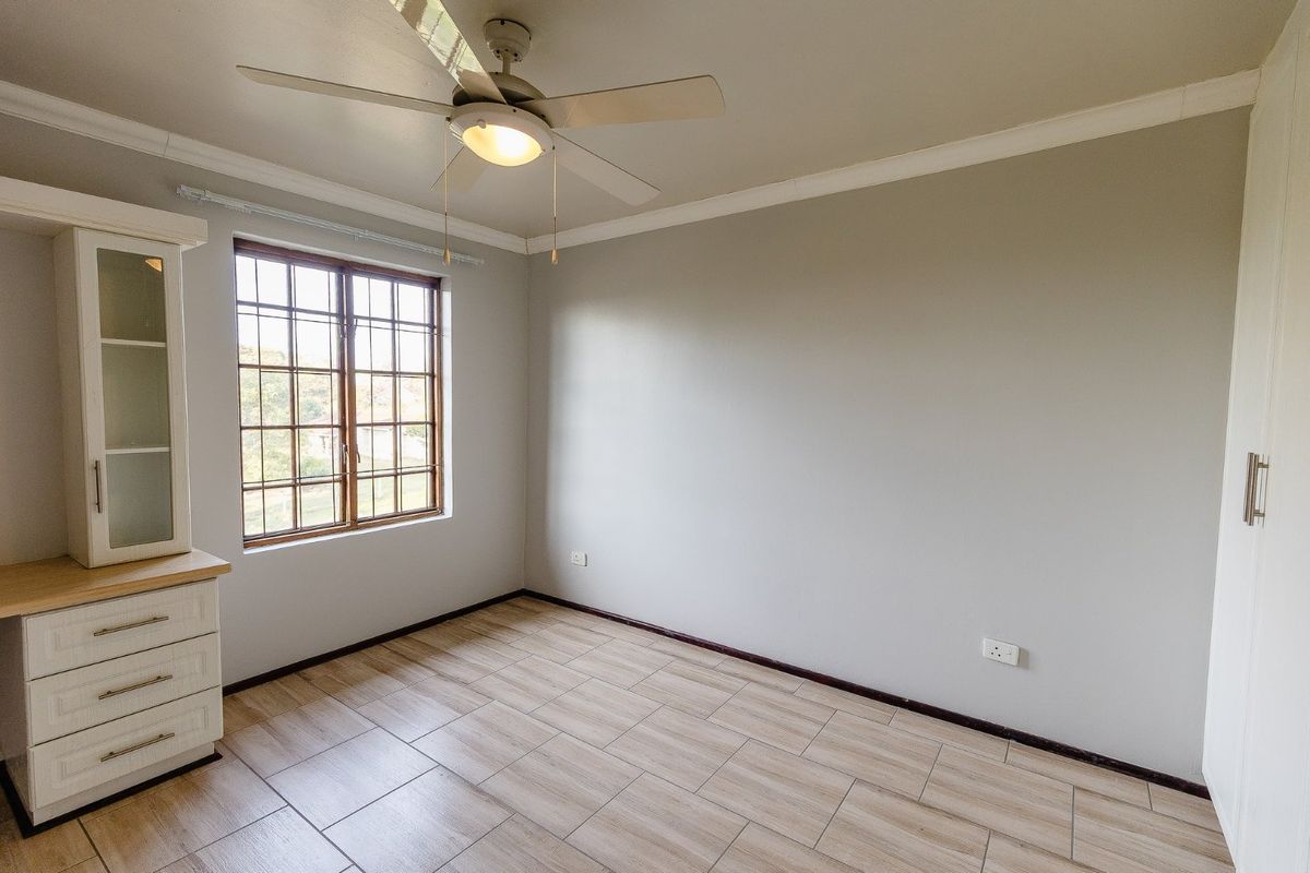A bright, empty bedroom featuring tiled flooring, a ceiling fan, and built-in cabinetry, offering a clean and neutral space ready for personalization.