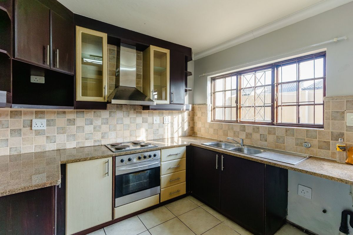A functional kitchen featuring dark and light cabinetry, granite countertops, a built-in oven with extractor fan, and a double basin sink with tiled backsplash.