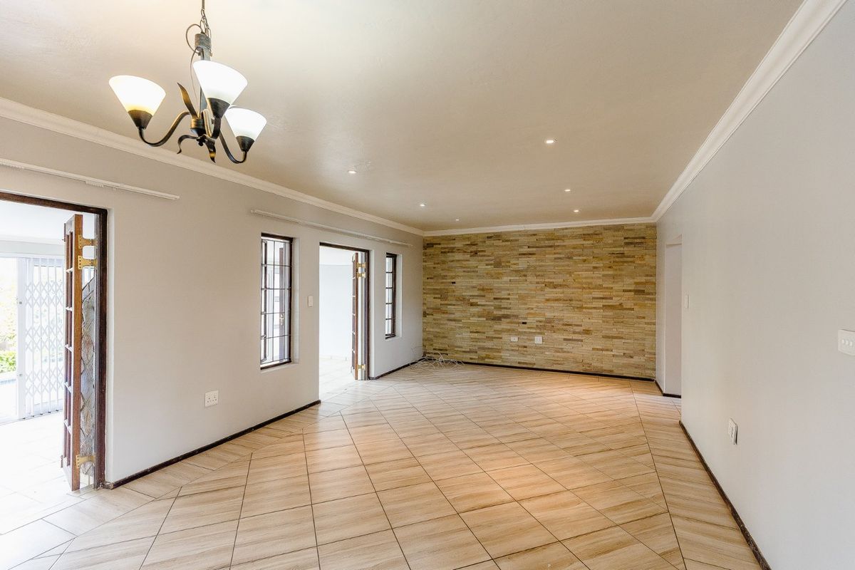 Spacious, light-filled living area featuring neutral tiled flooring, a decorative stone feature wall, and elegant lighting fixtures, offering a versatile open-plan layout.