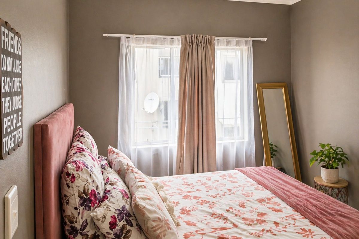 A cozy bedroom featuring neutral wall tones, a window with curtain rod, and standard electrical fixtures.