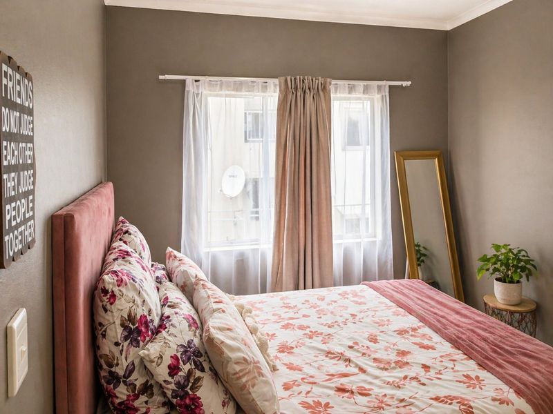 A cozy bedroom featuring neutral wall tones, a window with curtain rod, and standard electrical fixtures.