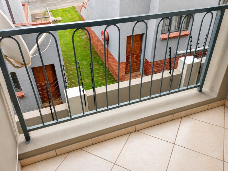 A clean, tiled balcony featuring a metal balustrade, overlooking a residential courtyard area with electric fencing.