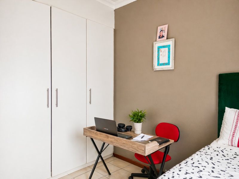 A bedroom featuring built-in white cupboards, tiled flooring, and a neutral accent wall.