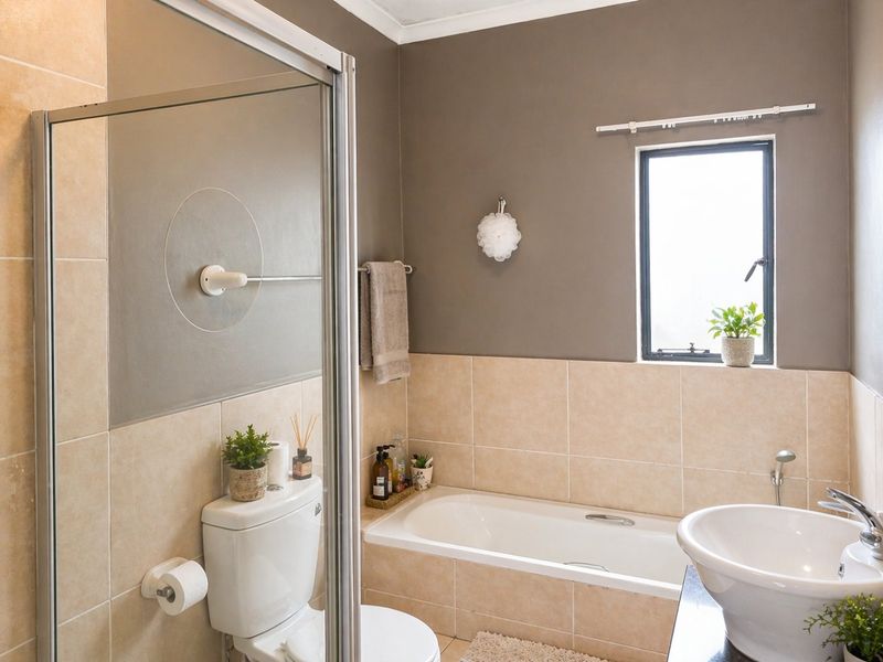 A well-maintained bathroom featuring a shower enclosure, a bathtub, and a pedestal basin with neutral wall tiling.