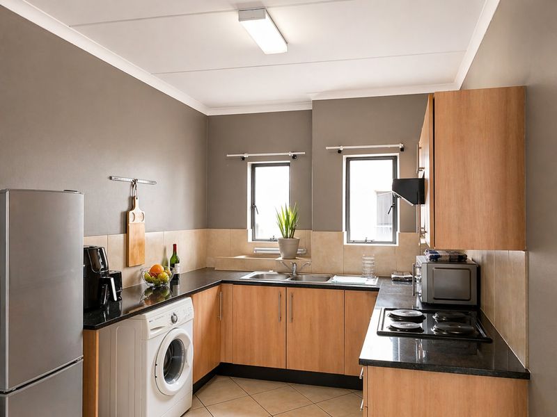 Functional kitchen featuring laminate cabinetry, granite countertops, a double basin sink, built-in electric hob, extractor fan, and integrated laundry plumbing.