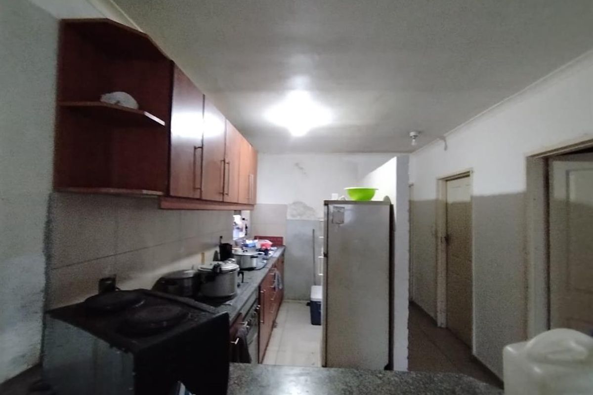 A functional kitchen featuring built-in wooden cabinetry, stone countertops, and a hob, currently showing signs of wear and requiring cosmetic updates.