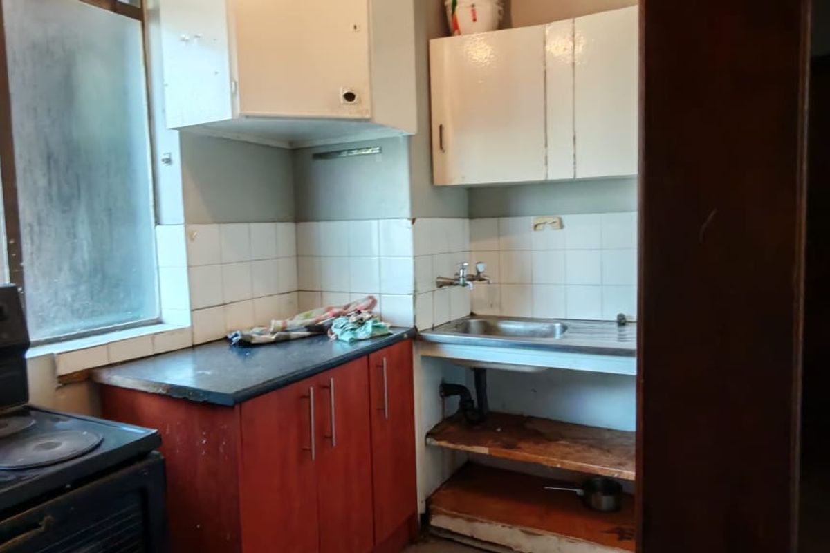 A dated kitchen featuring basic cabinetry, a stainless steel sink, and an electric stove, requiring modernization and cosmetic updates to improve functionality and aesthetic appeal.