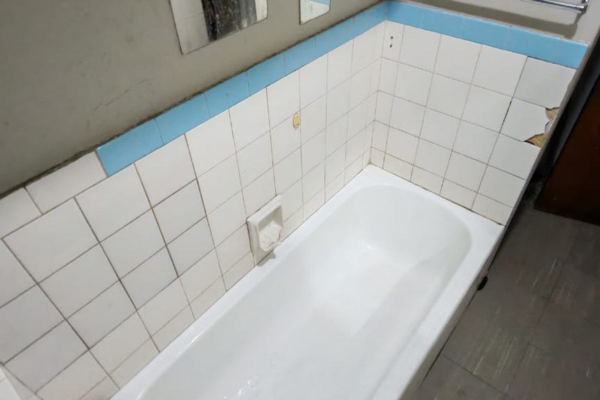 A dated bathroom featuring a built-in bathtub with damaged and missing ceramic wall tiles, requiring renovation to restore the space.