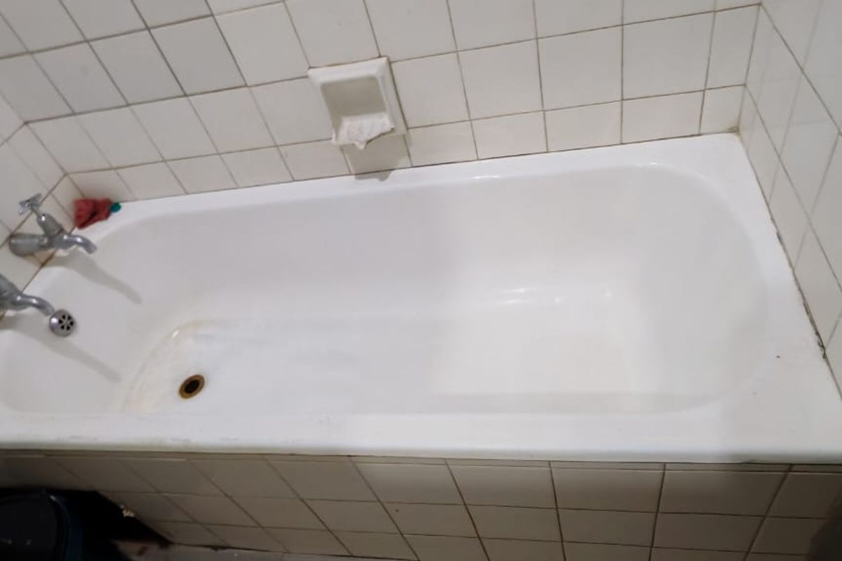 A dated bathroom featuring a built-in bathtub with ceramic wall tiling and traditional chrome faucets, requiring cosmetic updates and surface restoration.