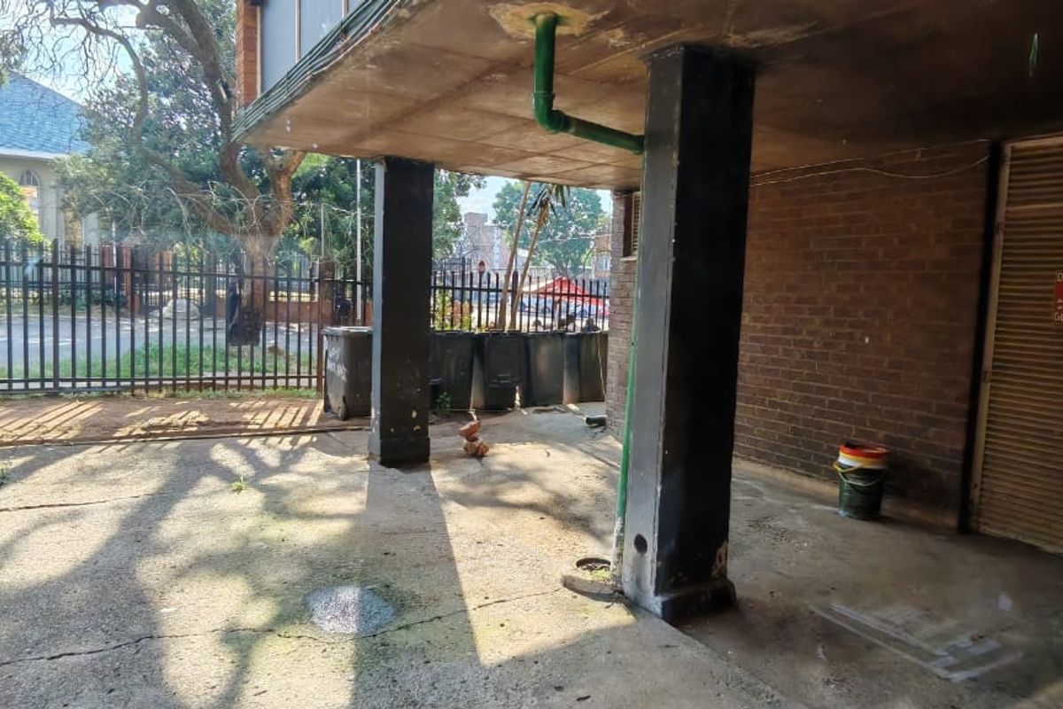 A rear exterior area featuring concrete paving, brick walls, and a metal security fence, showing signs of wear and weathering.