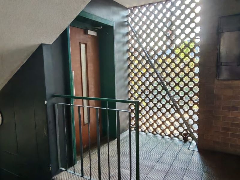 A communal apartment hallway featuring a decorative breeze block screen, metal balustrade, and a built-in refuse chute door.