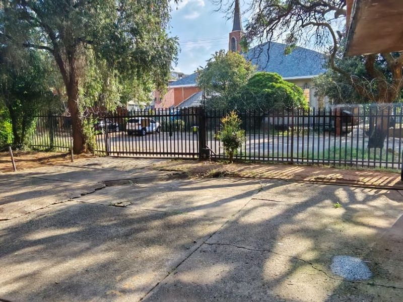 Exterior view of the property entrance featuring a concrete driveway, metal security fencing, and perimeter security measures.