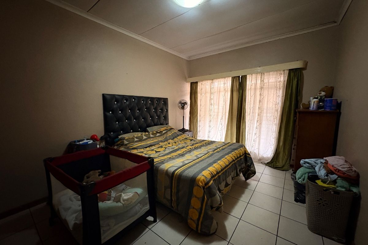 A bedroom featuring tiled flooring, a ceiling-mounted light fixture, and large windows with curtain rails, providing natural light to the space.