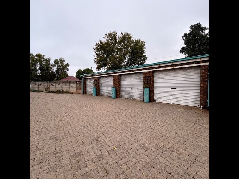 A row of secure garage units featuring roller shutter doors and a paved driveway area within a residential complex.