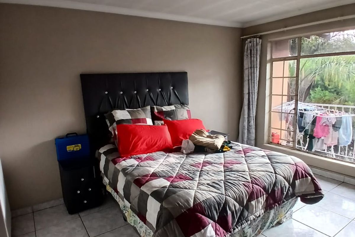 A bedroom featuring tiled flooring, a central ceiling light, and a large window providing natural light and a view of the exterior.